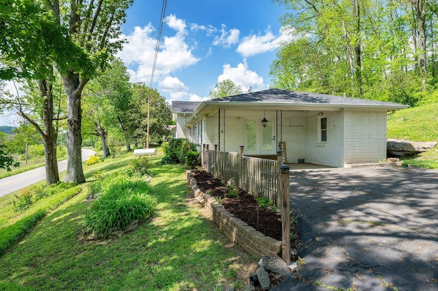 view of side of property with brick siding, aphalt driveway, a lawn, and an attached carport