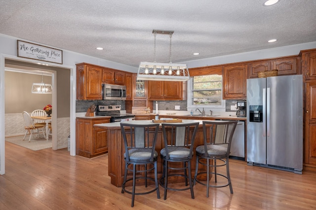 kitchen with an island with sink, a textured ceiling, appliances with stainless steel finishes, and brown cabinets