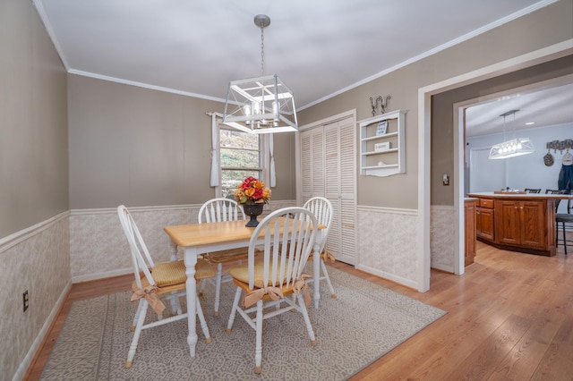 dining space featuring a chandelier, ornamental molding, light wood-style flooring, and a wainscoted wall