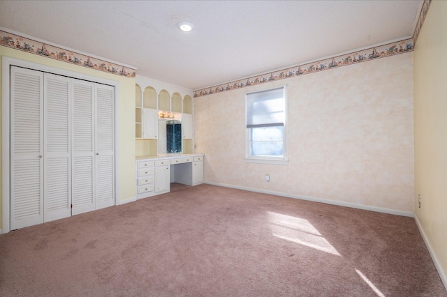 unfurnished bedroom featuring built in study area, baseboards, light carpet, and a closet