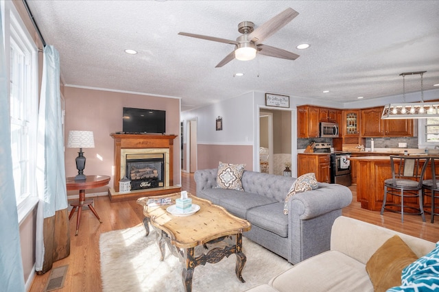 living area with light wood-style floors, a textured ceiling, ceiling fan, and visible vents