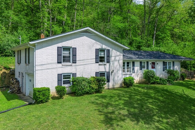 split level home featuring a view of trees, a chimney, a front lawn, and a garage
