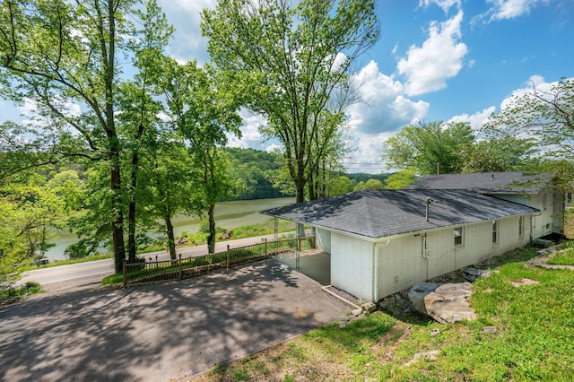 view of home's exterior featuring a shingled roof, fence, driveway, and a carport