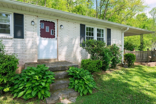 view of exterior entry featuring a lawn, brick siding, and fence