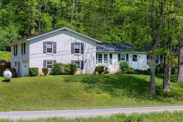 tri-level home featuring brick siding, an attached garage, a chimney, and a front lawn