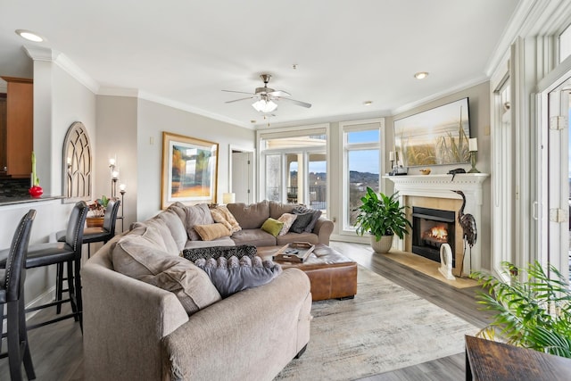 living room featuring ornamental molding, hardwood / wood-style flooring, a tile fireplace, and ceiling fan