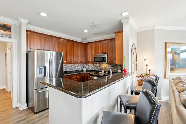 kitchen featuring a breakfast bar area, stainless steel appliances, kitchen peninsula, backsplash, and dark stone countertops