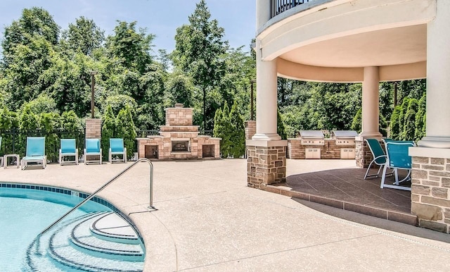 view of patio / terrace featuring exterior kitchen, a balcony, a community pool, grilling area, and an outdoor stone fireplace