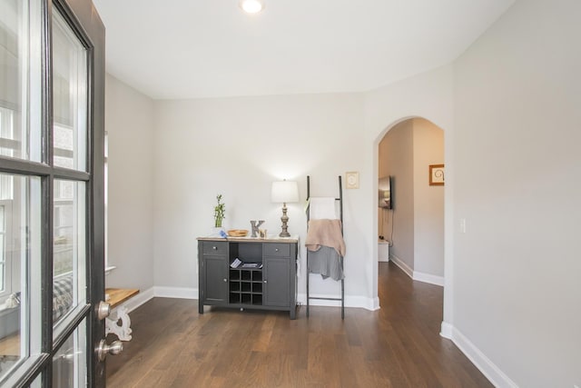 interior space with baseboards, arched walkways, and dark wood-type flooring