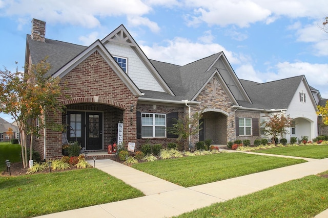 craftsman-style house with a shingled roof, a front yard, a chimney, and brick siding