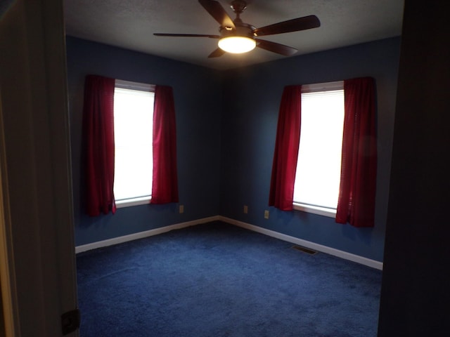 spare room featuring dark carpet, plenty of natural light, and ceiling fan