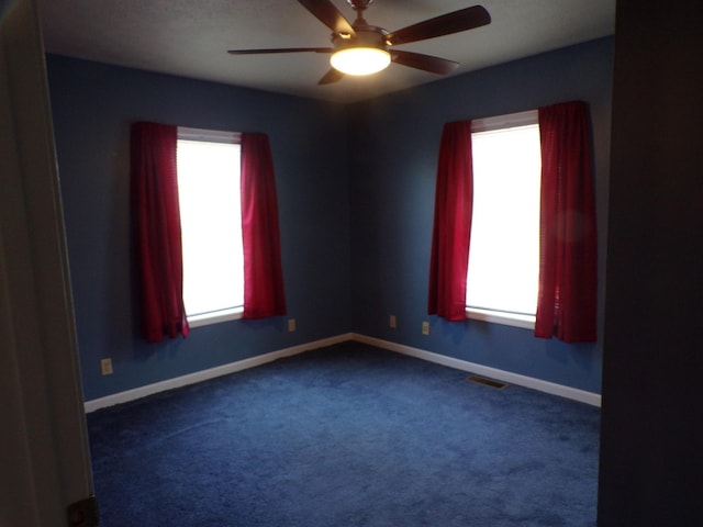 spare room featuring ceiling fan, dark colored carpet, and a wealth of natural light