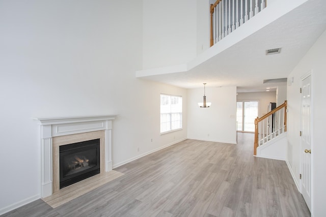 unfurnished living room with a high ceiling, a fireplace with flush hearth, baseboards, stairway, and light wood-type flooring