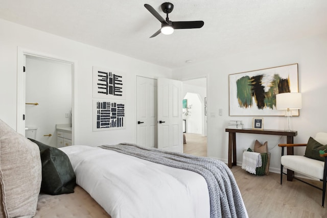 bedroom featuring baseboards, ceiling fan, ensuite bath, and light wood finished floors