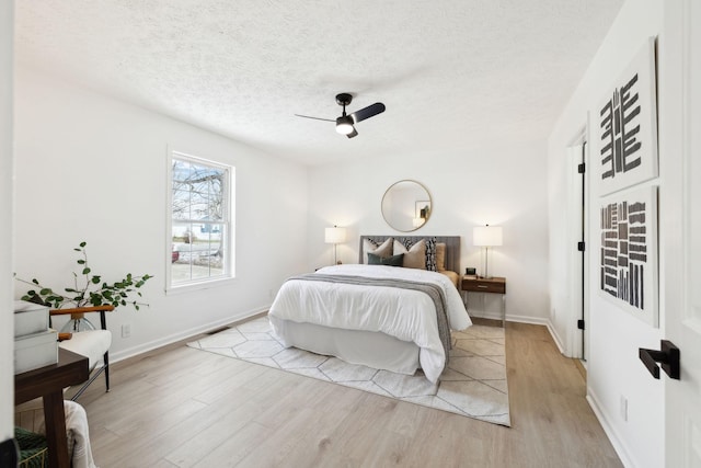 bedroom featuring a ceiling fan, light wood-type flooring, a textured ceiling, and baseboards