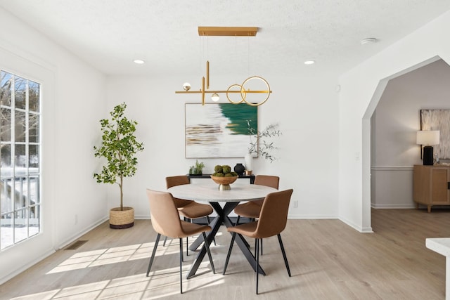 dining area with a healthy amount of sunlight, light wood-style floors, and arched walkways