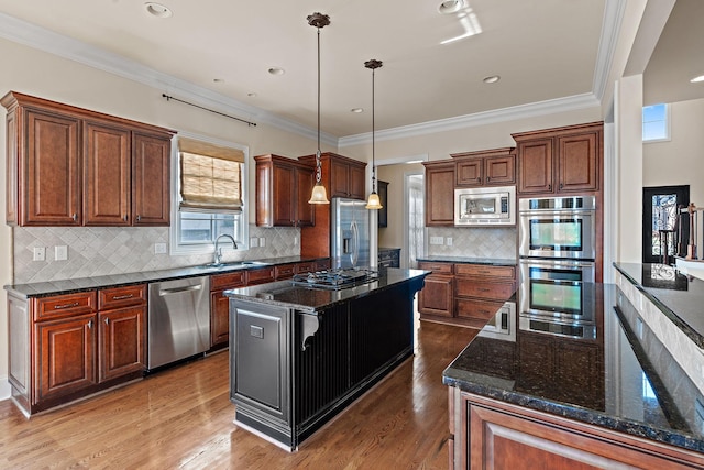 kitchen featuring hanging light fixtures, stainless steel appliances, a center island, sink, and dark stone countertops