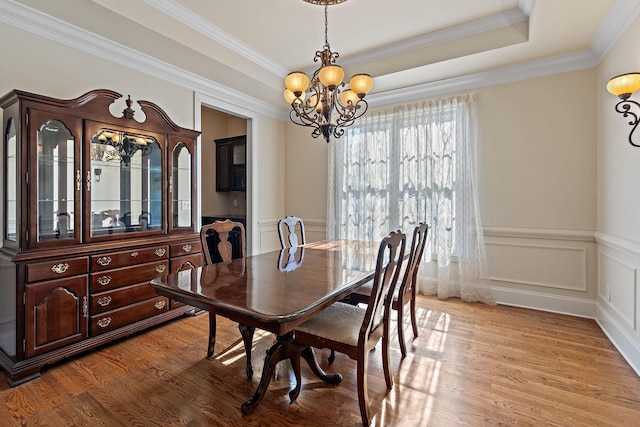 dining room featuring a raised ceiling, light hardwood / wood-style flooring, crown molding, and a notable chandelier