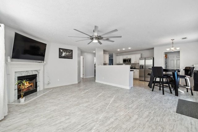 living room with ceiling fan with notable chandelier, light hardwood / wood-style flooring, a textured ceiling, and a fireplace