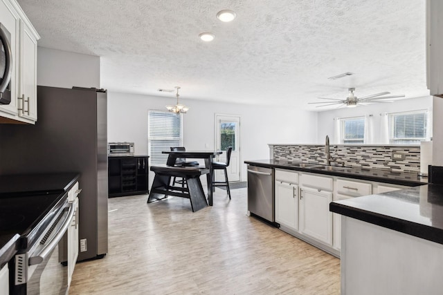 kitchen with appliances with stainless steel finishes, hanging light fixtures, backsplash, sink, and white cabinetry