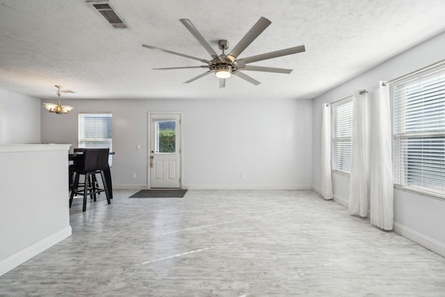 unfurnished living room with ceiling fan with notable chandelier, light hardwood / wood-style floors, a textured ceiling, and a wealth of natural light