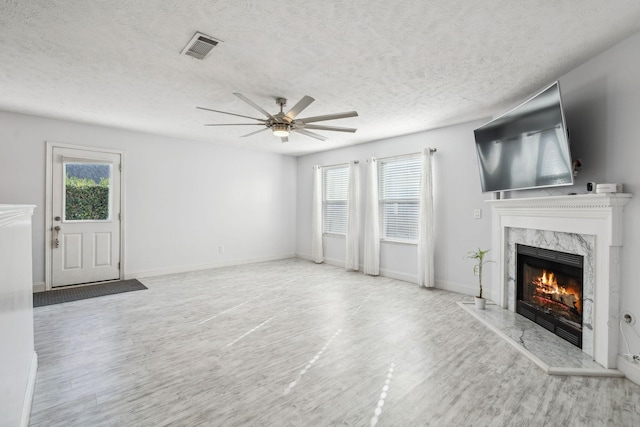 unfurnished living room with light wood-type flooring, ceiling fan, a textured ceiling, and a fireplace