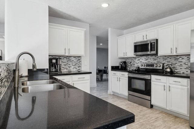 kitchen featuring appliances with stainless steel finishes, light wood-type flooring, backsplash, sink, and white cabinetry