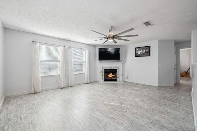 unfurnished living room with a fireplace, a textured ceiling, ceiling fan, and light hardwood / wood-style flooring