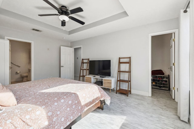 bedroom featuring light hardwood / wood-style flooring, ensuite bathroom, a raised ceiling, and a spacious closet