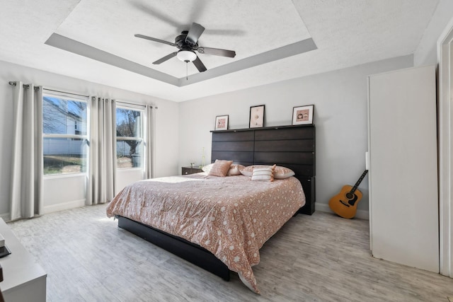 bedroom with a tray ceiling, light hardwood / wood-style flooring, a textured ceiling, and ceiling fan