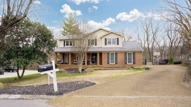 view of front of property with concrete driveway, brick siding, a chimney, and covered porch