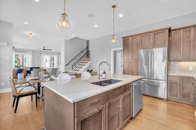 kitchen featuring a center island with sink, appliances with stainless steel finishes, sink, light stone counters, and decorative light fixtures