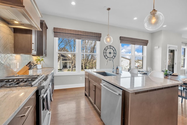 kitchen featuring a center island with sink, appliances with stainless steel finishes, sink, premium range hood, and pendant lighting