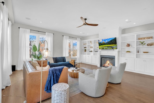 living room featuring built in features, ceiling fan, and light hardwood / wood-style flooring