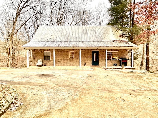 farmhouse-style home with a porch, brick siding, and metal roof