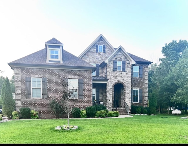 craftsman house featuring a front yard, brick siding, and roof with shingles