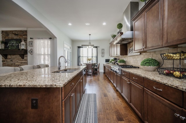 kitchen with dark wood finished floors, wall chimney exhaust hood, a sink, stainless steel appliances, and backsplash