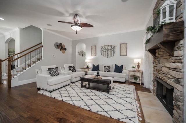 living area with arched walkways, a stone fireplace, and wood finished floors