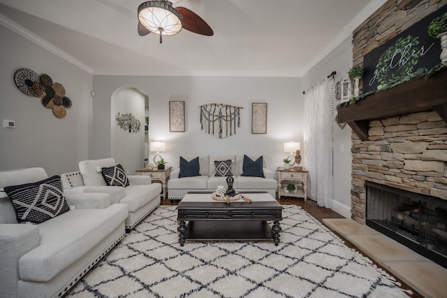 living room featuring arched walkways, a fireplace, crown molding, a ceiling fan, and wood finished floors