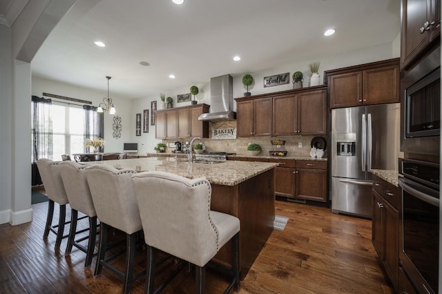 kitchen featuring dark wood-style flooring, a sink, stainless steel appliances, wall chimney range hood, and backsplash