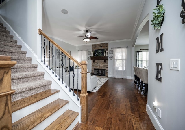 foyer entrance with dark wood-style floors, stairway, ornamental molding, a stone fireplace, and baseboards