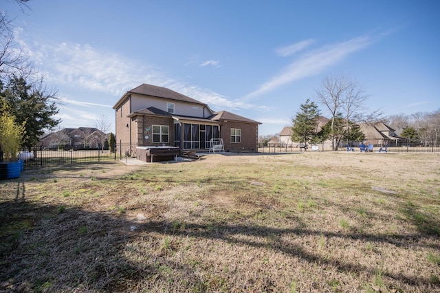 back of house with a sunroom, a fenced backyard, a jacuzzi, a yard, and brick siding