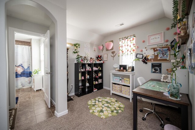 carpeted home office featuring baseboards, visible vents, arched walkways, lofted ceiling, and tile patterned floors