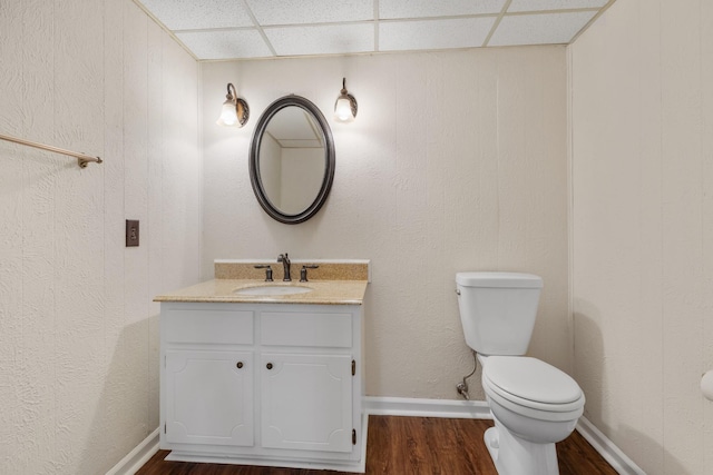 bathroom featuring toilet, vanity, hardwood / wood-style floors, and a drop ceiling