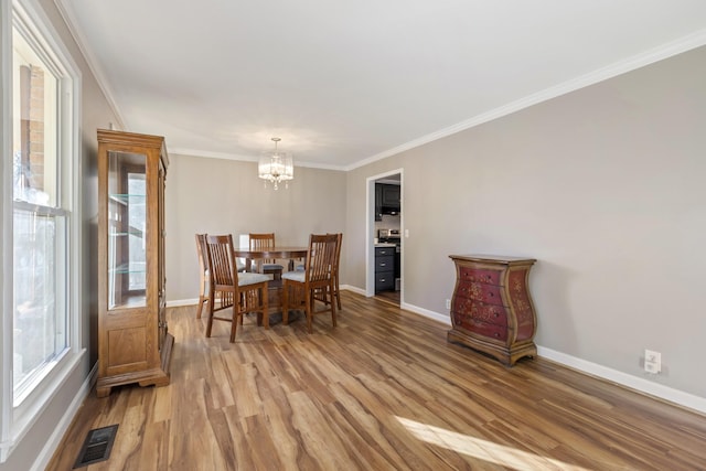 dining space with light wood-type flooring, an inviting chandelier, and crown molding