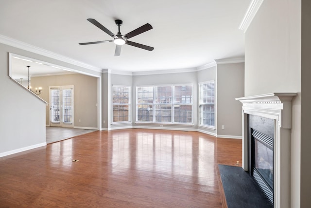 unfurnished living room with baseboards, ornamental molding, wood finished floors, a fireplace, and ceiling fan with notable chandelier