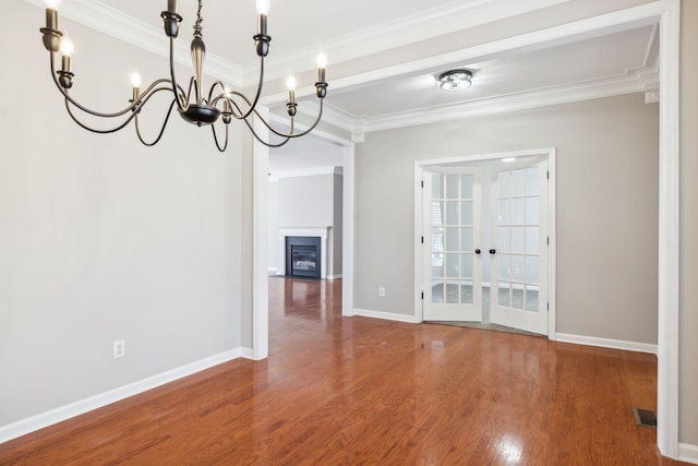 unfurnished dining area with french doors, a fireplace, ornamental molding, wood finished floors, and baseboards