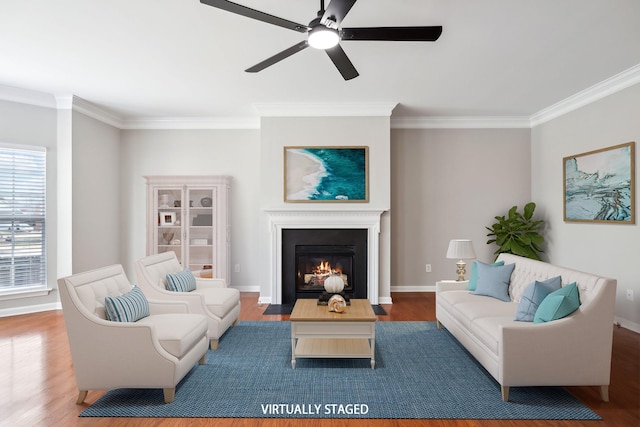 living area featuring ceiling fan, wood finished floors, a fireplace with flush hearth, baseboards, and crown molding