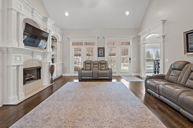 living room featuring high vaulted ceiling, ornate columns, dark wood-type flooring, and a fireplace