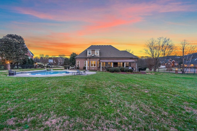 back house at dusk featuring a yard, a patio area, and a fenced in pool